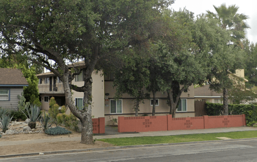 A tree in front of a house with a red fence.
